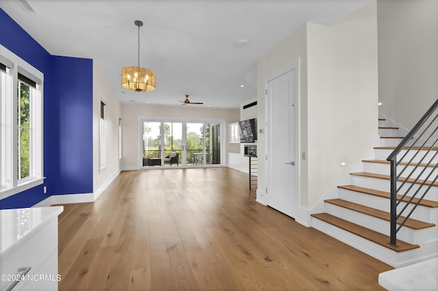 unfurnished living room with plenty of natural light, light wood-style flooring, stairs, and an inviting chandelier