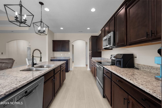 kitchen with light stone countertops, appliances with stainless steel finishes, sink, hanging light fixtures, and light hardwood / wood-style floors