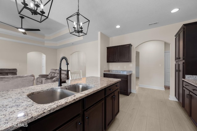 kitchen with ceiling fan, light wood-type flooring, sink, pendant lighting, and light stone counters