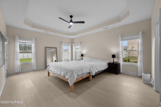 bedroom with ceiling fan, a raised ceiling, multiple windows, and light wood-type flooring