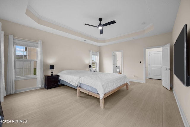 bedroom with ceiling fan, a raised ceiling, light hardwood / wood-style flooring, ornamental molding, and ensuite bathroom