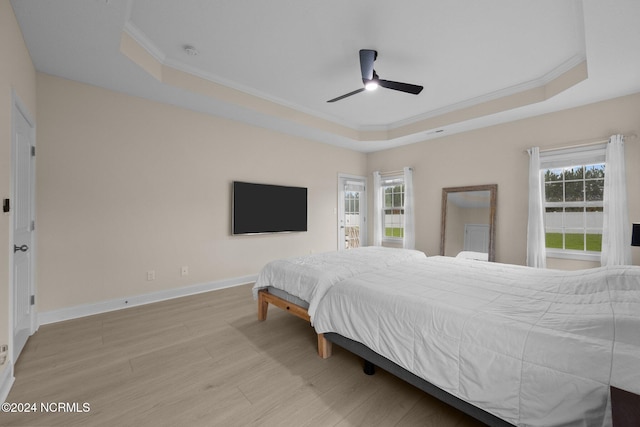 bedroom with light hardwood / wood-style floors, multiple windows, a tray ceiling, and ceiling fan