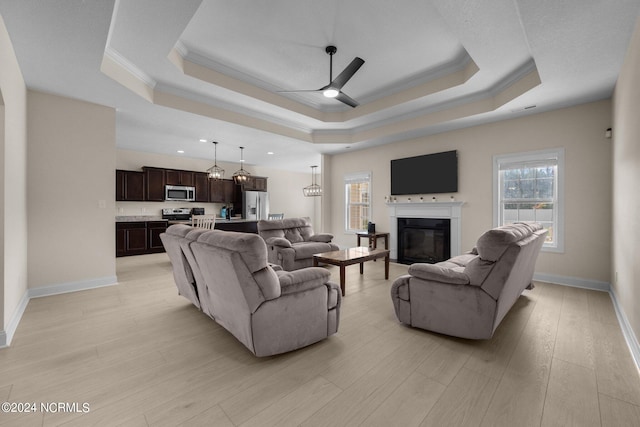 living room with ceiling fan, ornamental molding, light hardwood / wood-style floors, and a tray ceiling