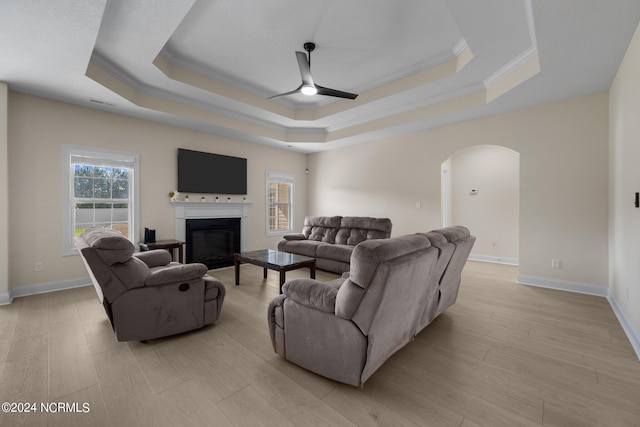 living room featuring ornamental molding, ceiling fan, light wood-type flooring, and a raised ceiling