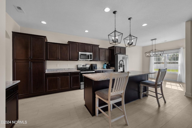 kitchen with an island with sink, hanging light fixtures, stainless steel appliances, a kitchen bar, and a notable chandelier