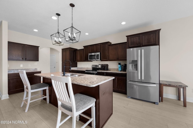 kitchen with a kitchen island with sink, a breakfast bar area, stainless steel appliances, sink, and decorative light fixtures