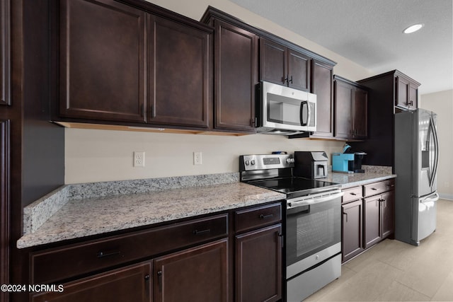 kitchen with light stone countertops, a textured ceiling, appliances with stainless steel finishes, and dark brown cabinetry