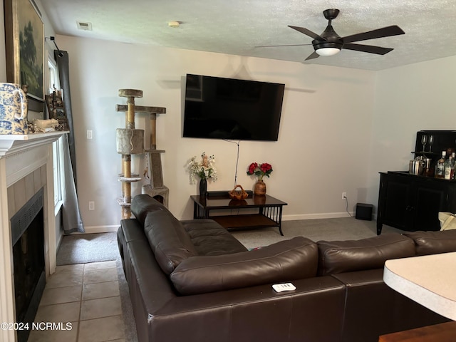 living room featuring a textured ceiling, a tiled fireplace, light tile patterned floors, and ceiling fan