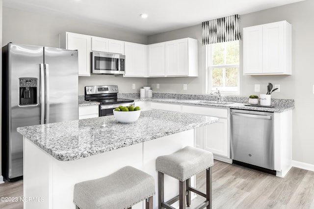 kitchen with white cabinets, a breakfast bar area, a kitchen island, light hardwood / wood-style floors, and appliances with stainless steel finishes