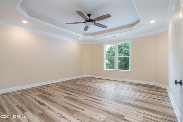 empty room featuring light wood-style flooring, baseboards, a raised ceiling, and ornamental molding