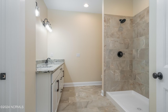 full bathroom with double vanity, tiled shower, a sink, and baseboards