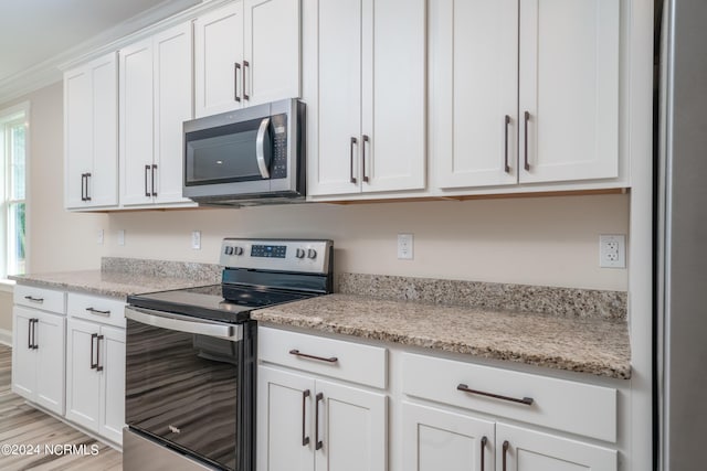 kitchen with stainless steel appliances, white cabinetry, light wood-style floors, ornamental molding, and light stone countertops