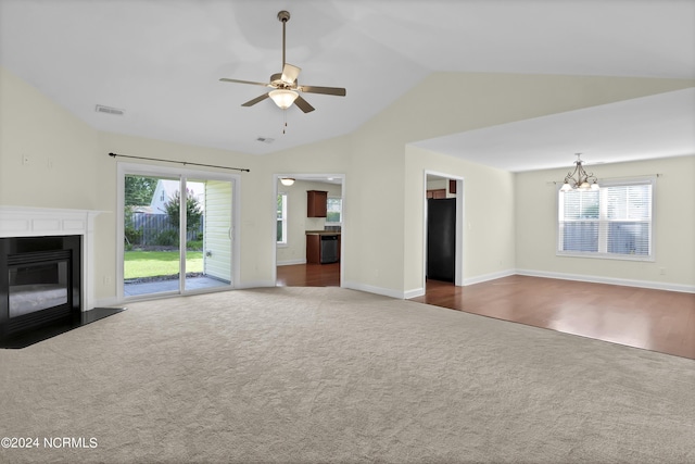 unfurnished living room featuring ceiling fan with notable chandelier, dark carpet, a fireplace with flush hearth, and a wealth of natural light