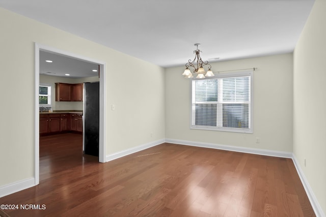 unfurnished dining area with dark wood-type flooring, recessed lighting, baseboards, and an inviting chandelier