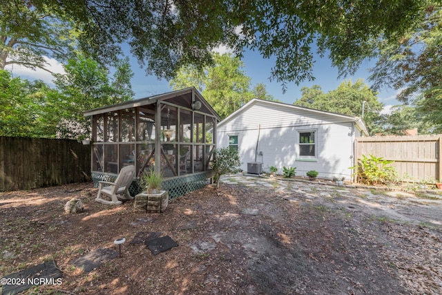 rear view of house with central AC unit, a fenced backyard, and a sunroom