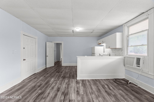 kitchen with dark wood-type flooring, kitchen peninsula, white cabinetry, and a drop ceiling