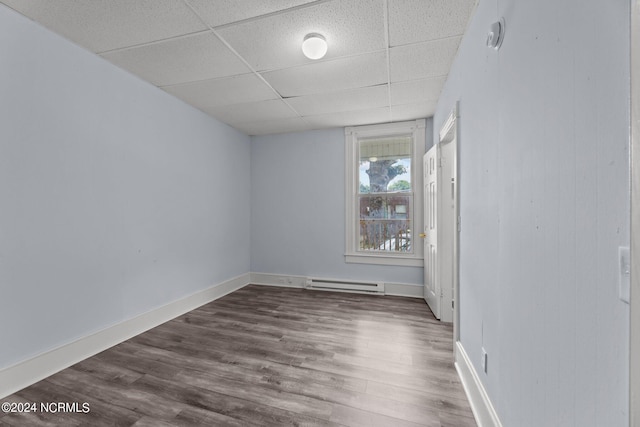 empty room with dark wood-type flooring, a paneled ceiling, and baseboard heating