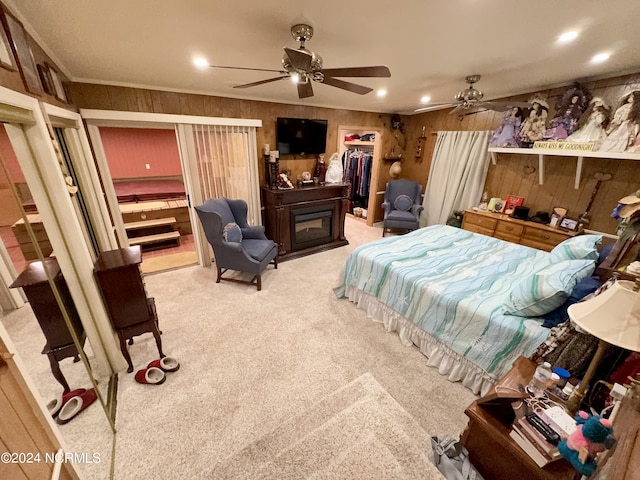 bedroom featuring light colored carpet, a spacious closet, ornamental molding, a glass covered fireplace, and ceiling fan