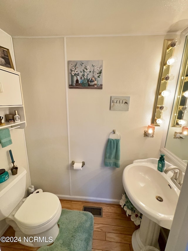 half bath with visible vents, toilet, a sink, wood finished floors, and baseboards