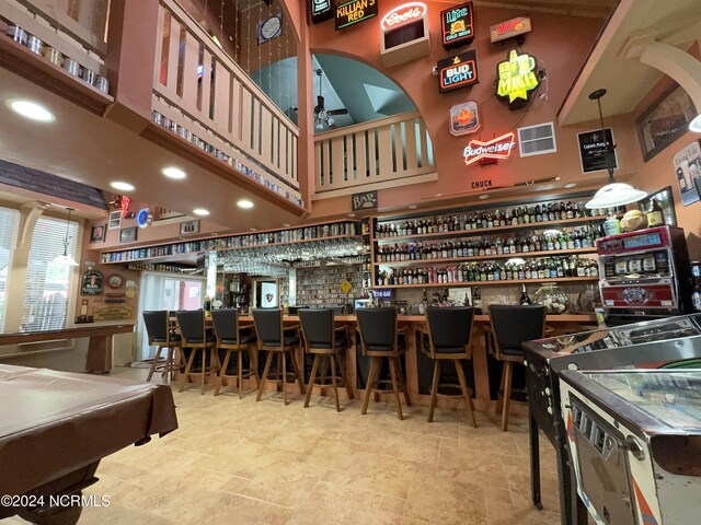 bar with light tile patterned floors, pool table, a towering ceiling, and hanging light fixtures