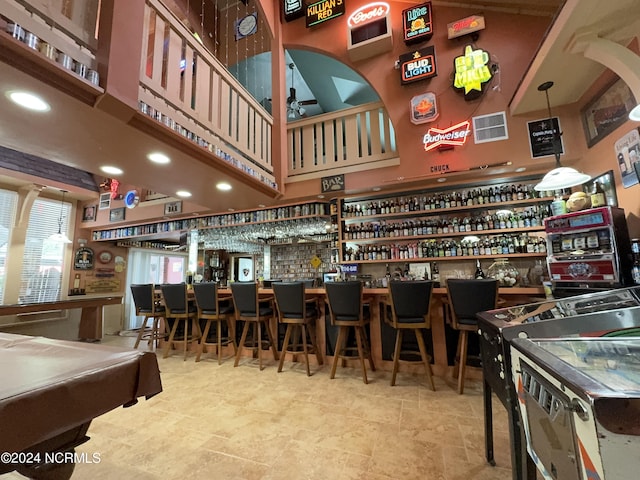 interior space with a community bar, ceiling fan, a high ceiling, and stone finish floor