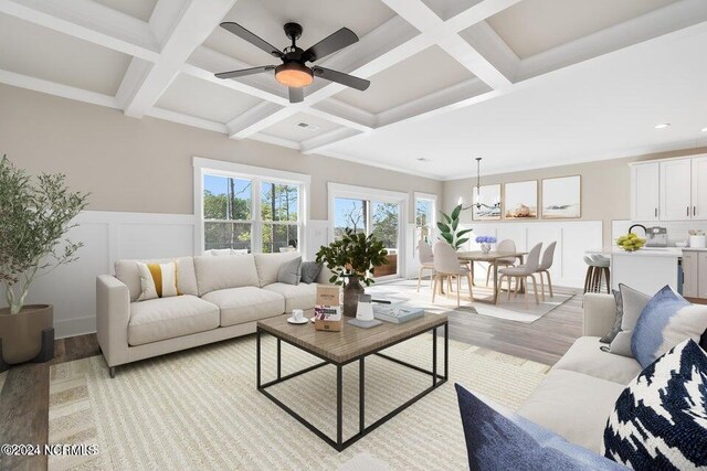 living room with beam ceiling, ceiling fan with notable chandelier, light hardwood / wood-style floors, and coffered ceiling