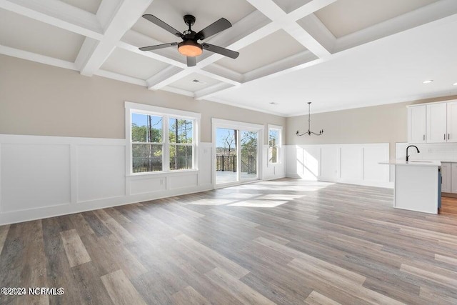 unfurnished living room with coffered ceiling, beamed ceiling, light wood-style flooring, and a sink