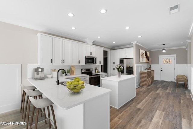 kitchen featuring a center island, light countertops, visible vents, appliances with stainless steel finishes, and wainscoting