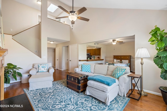 living room featuring light hardwood / wood-style flooring, high vaulted ceiling, a skylight, and ceiling fan