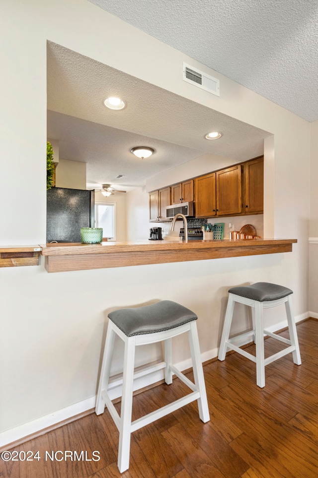 kitchen featuring kitchen peninsula, a breakfast bar area, dark hardwood / wood-style flooring, a textured ceiling, and refrigerator