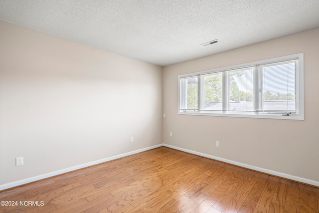 spare room with a textured ceiling and light hardwood / wood-style flooring