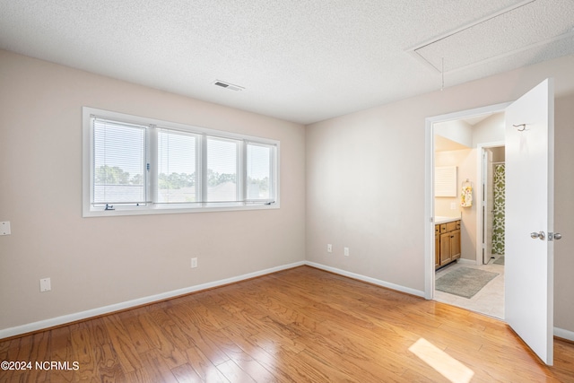 unfurnished bedroom with connected bathroom, a textured ceiling, and light hardwood / wood-style floors