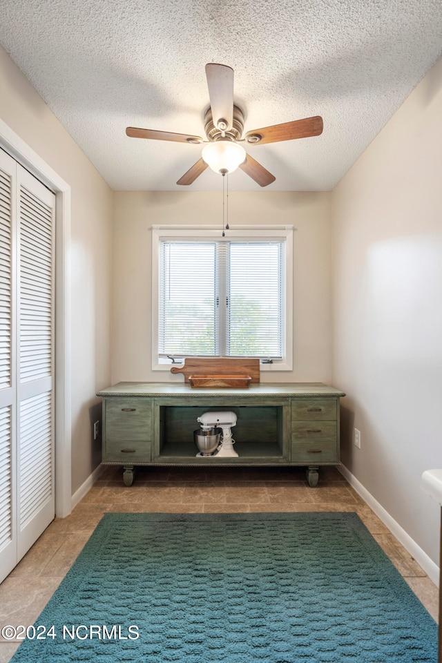 unfurnished office with dark tile patterned flooring, a textured ceiling, and ceiling fan