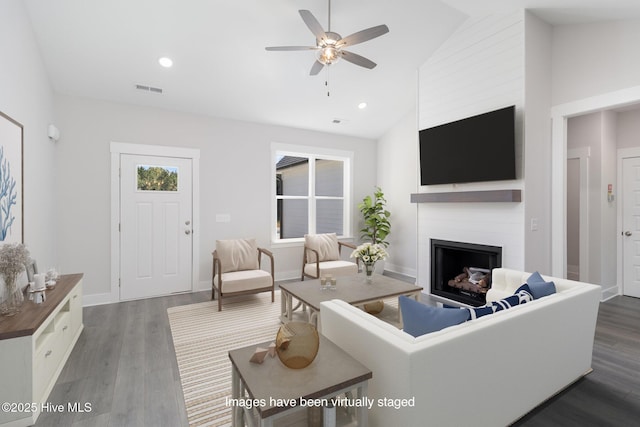living room featuring dark wood-type flooring, a large fireplace, ceiling fan, and high vaulted ceiling