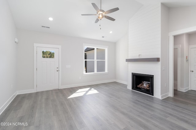 unfurnished living room with ceiling fan, high vaulted ceiling, a large fireplace, and light wood-type flooring