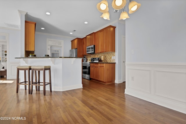 kitchen featuring light wood-type flooring, a breakfast bar, dark stone countertops, kitchen peninsula, and appliances with stainless steel finishes