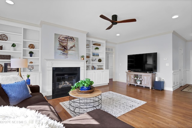 living room featuring dark wood-type flooring, crown molding, built in shelves, and ceiling fan