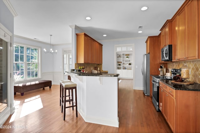 kitchen featuring light wood-type flooring, dark stone counters, a kitchen breakfast bar, decorative backsplash, and appliances with stainless steel finishes