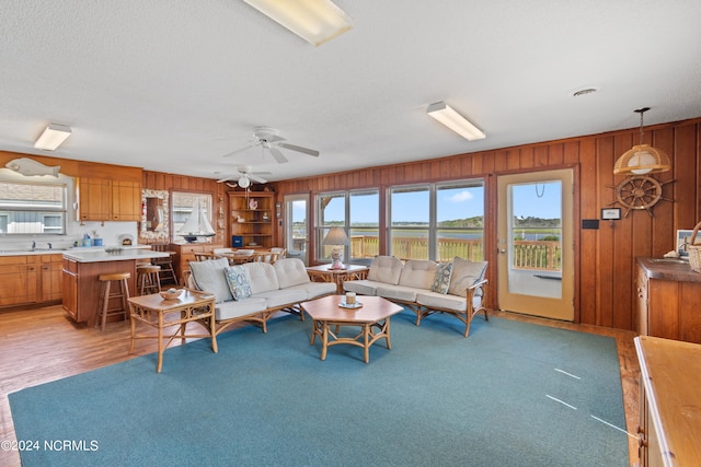 living room featuring ceiling fan, wooden walls, hardwood / wood-style floors, and a textured ceiling