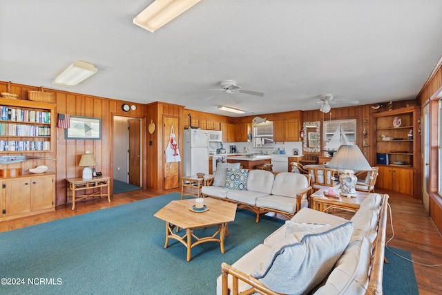 living room with ceiling fan, hardwood / wood-style flooring, wooden walls, and built in shelves