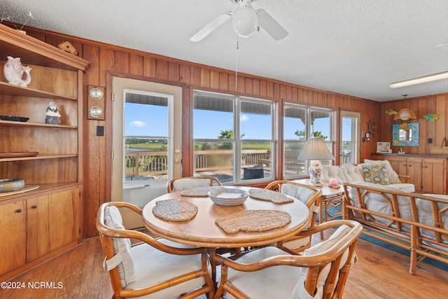 dining area featuring light wood-type flooring, ceiling fan, wooden walls, and a textured ceiling