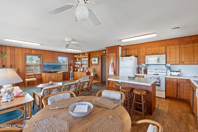 dining room with ceiling fan, wooden walls, a textured ceiling, and dark hardwood / wood-style flooring