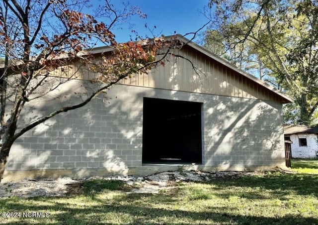 view of side of home with a detached garage, concrete block siding, a lawn, and an outbuilding