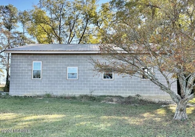 view of home's exterior with concrete block siding, a lawn, and metal roof