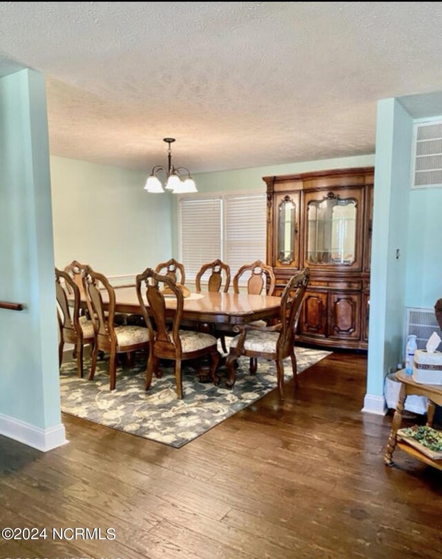 dining room featuring dark wood-type flooring, a textured ceiling, baseboards, and a chandelier