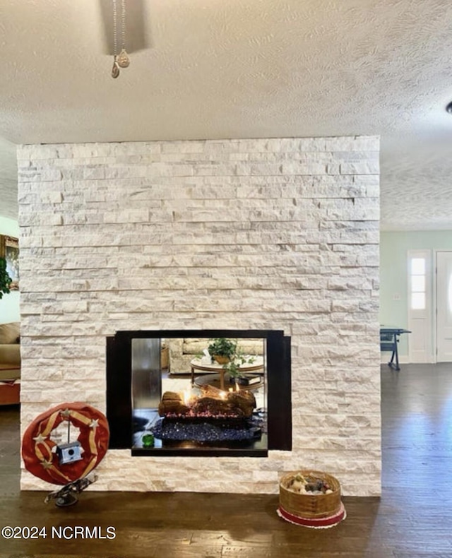 detailed view of a textured ceiling, wood finished floors, a stone fireplace, and baseboards