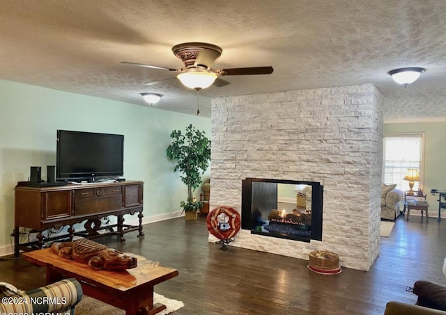 living room with a ceiling fan, a stone fireplace, a textured ceiling, wood finished floors, and baseboards