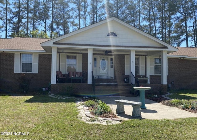 view of front facade with covered porch, roof with shingles, a front yard, and brick siding