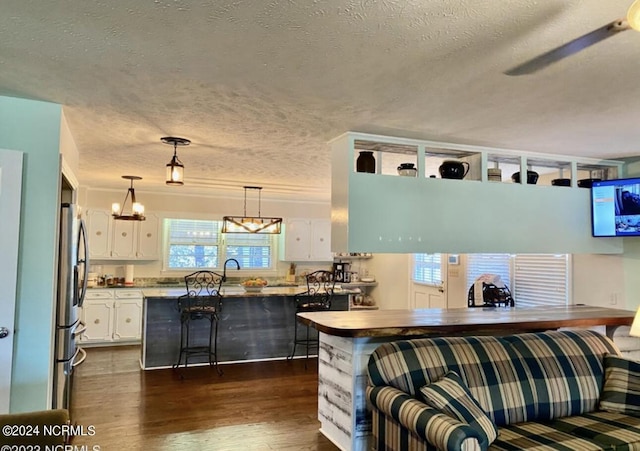 kitchen with dark wood-style flooring, light countertops, hanging light fixtures, white cabinetry, and stainless steel fridge with ice dispenser