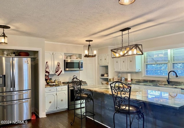 kitchen with stainless steel appliances, a sink, white cabinets, dark wood-style flooring, and a breakfast bar area